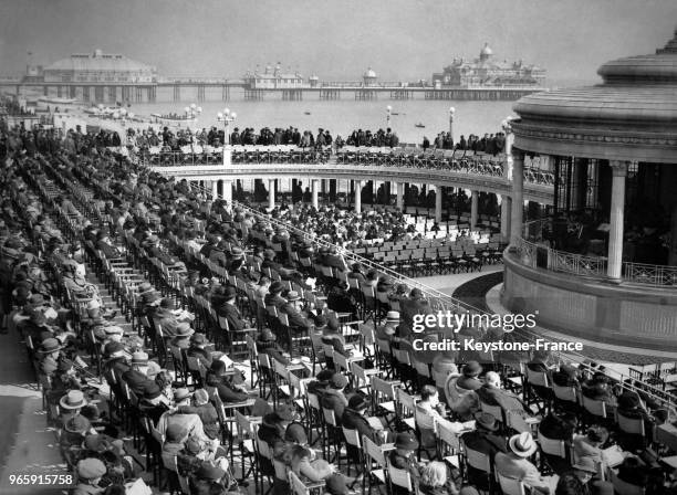 Des spectateurs profitent du beau temps pour écouter un concert donné par les Scots Guards royaux dans un kiosque du front de mer le 26 mars 1937 à...