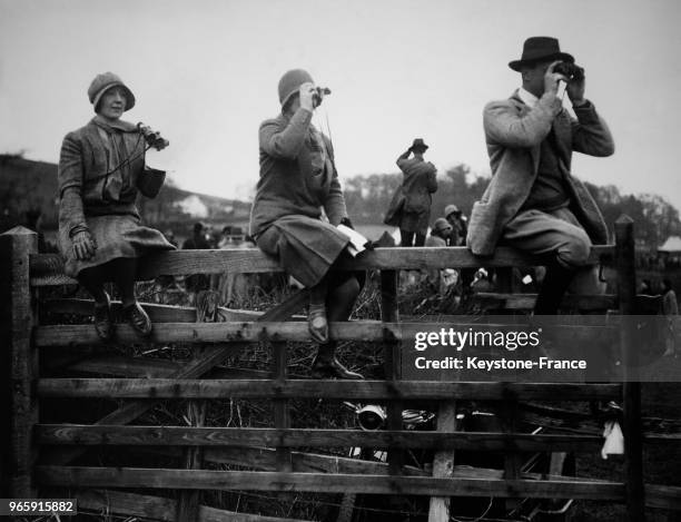Des spectateurs assis sur une barrière regardent la course à travers leurs jumelles, à Northampton, Royaume-Uni le 25 mars 1930.