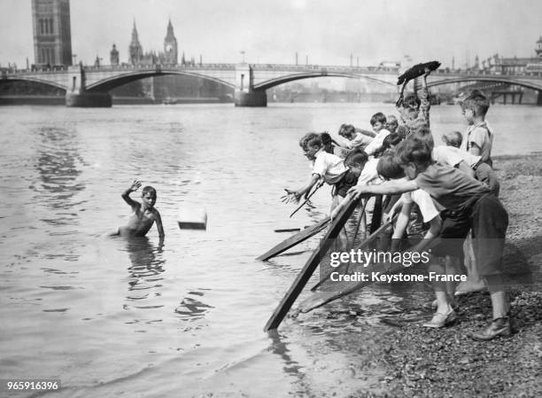 Nettoyage de la Tamise par des enfants, un garçon dans l'eau récupère les bouts de bois et les lance à ses camarades restés sur la rive, à Londres,...