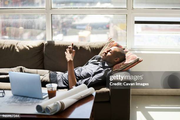 businessman using smart phone while lying on sofa in creative office - roll call stock pictures, royalty-free photos & images