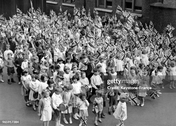 Des enfants portant des drapeaux britanniques sont réunis dans une cour d'une école à Londres, Royaume-Uni le 22 mai 1936.