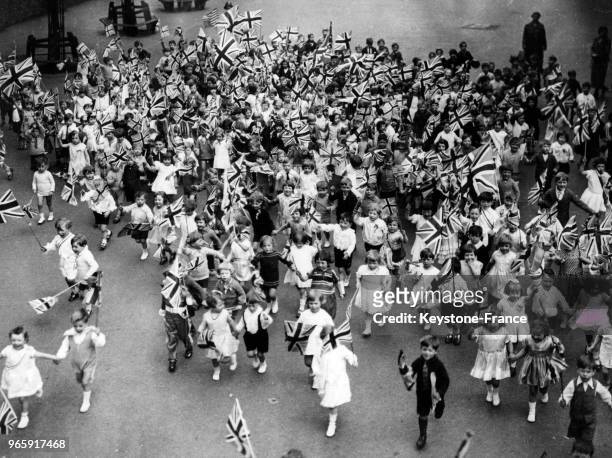 Des enfants courent avec le drapeau britannique dans les mains dans une cour de récréation d'une école à Londres, Royaume-Uni le 24 mai 1932.