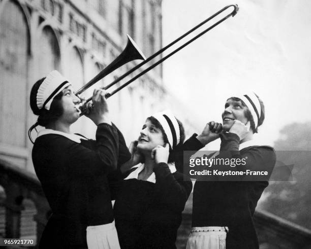 Deux jeunes femmes font mine de se boucher les oreilles pendant que leur comparse joue du trombone à coulisse en attendant de participer à un...