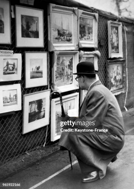 Un homme, accroupi, regarde de près les peintures présentées à Victoria Embankment, à Londres, Royaume-Uni le 28 avril 1958.