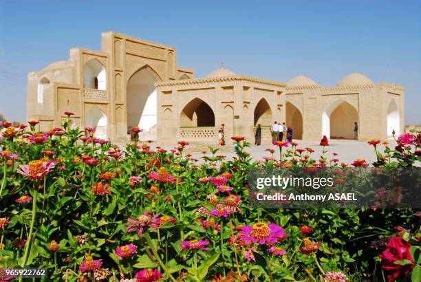 Flowers on plants with people standing outside ancient mosque in the background, Merv, Turkmenistan.