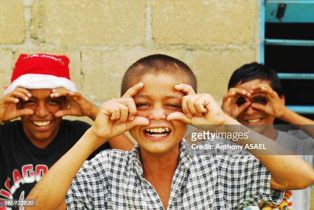Trois enfants imitant le geste de photographier, l'un d'eux porte un chapeau de Père Noel, Belise.
