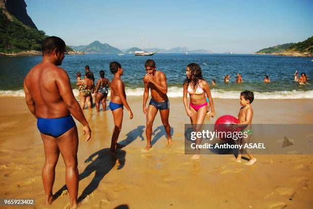 Brazil, Rio de Janeiro, Urca , families playing at the beach with Sugar Loaf in background.