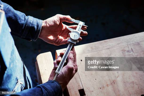 midsection of carpenter holding vernier caliper at table in workshop - vernier caliper stock-fotos und bilder