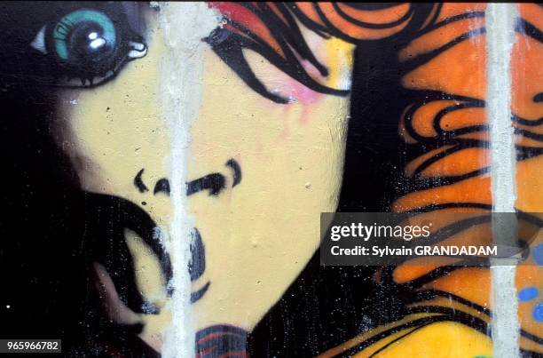 GERMANY.BERLIN.REMNANTS OF THE BERLIN WALL DRESSED WITH GRAFITTIS.CLOSE UP ON A FEMALE FACE.