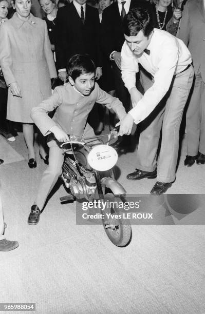 Reza Pahlavi essayant une moto pour enfant au salon du jouet le 13 février 1970 à Paris, France.