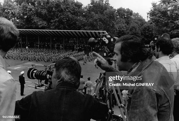 Le metteur en scène Jean Yanne derrière la caméra pour son prochain film sur les Champs Elysées, à Paris, France, durant le défilé du 14 juillet 1973.