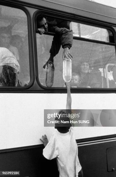 Enfant passant une bouteille d'eau au passager d'un car, lors de l'arrivée de réfugiés albanais du Kosovo à la gare routière de Blace, le 15 avril...