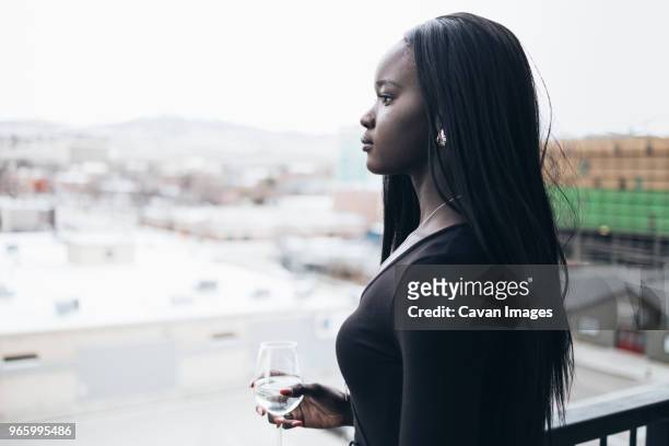 side view of thoughtful businesswoman holding drink while looking away in hotel balcony - straight hair fotografías e imágenes de stock