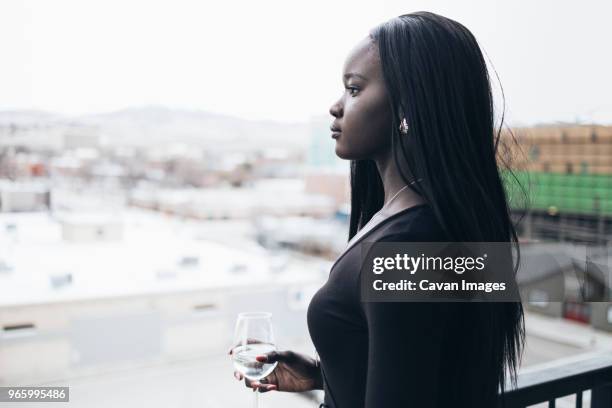 side view of thoughtful businesswoman holding drink while looking away in hotel balcony - woman with straight hair stock pictures, royalty-free photos & images