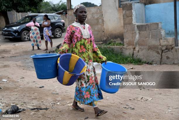 Woman carrying three large buckets arrives to receive water distributed by workers of the National Office of Drinking Water to the population on June...