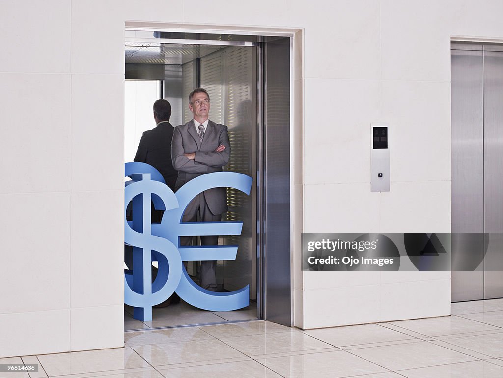 Businessman on elevator with dollar, euro and British pound symbols