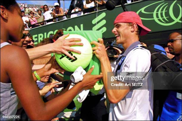 Grinning victorious tennis wunderkid Andy Roddick of Boca Raton, Florida, signs a big penn ball, with red baseball hat on backwards.