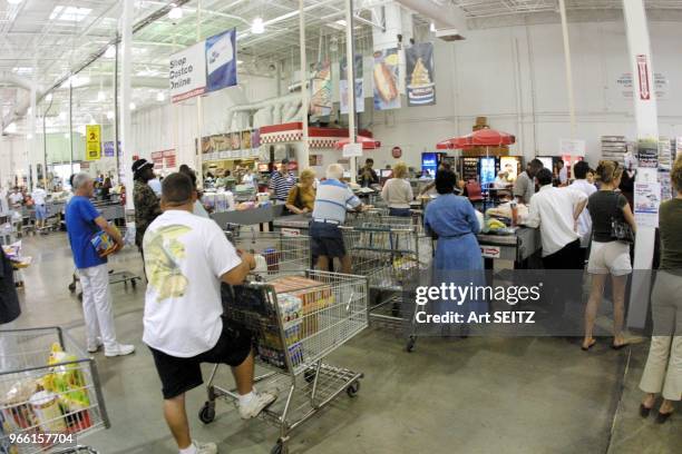 Costco Wholesale Warehouse-No frills bulk purchase shopping. Customers with shopping carts at checkout line. Costco on line sign is over head and...
