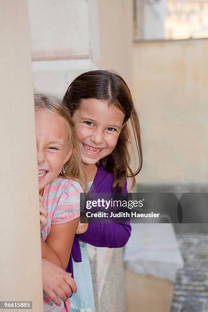 two girls hiding behind wall, laughing - taquiner photos et images de collection