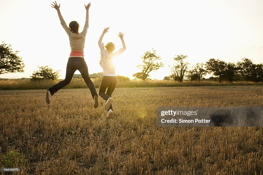 Two young girls leaping in a corn field