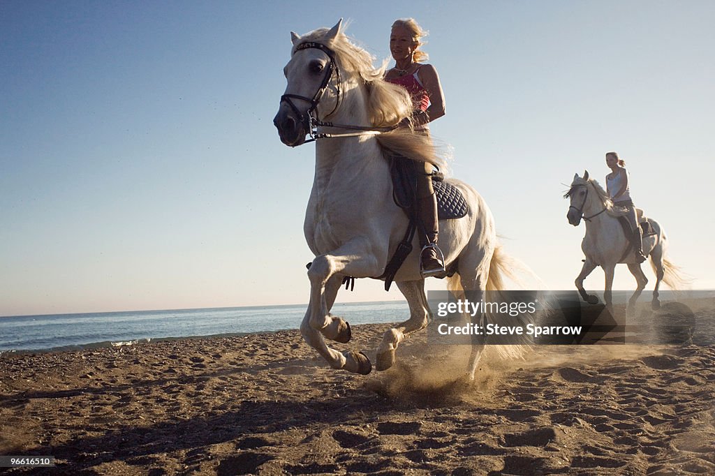 Two women riding horses on beach