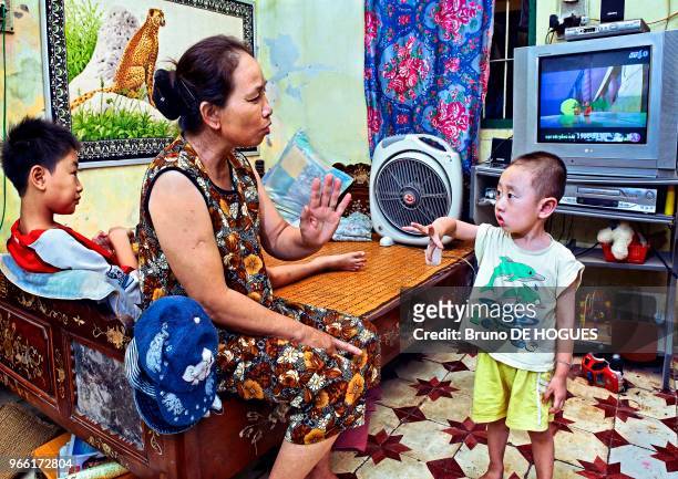 Une grand-mère s'occupant de ses petits-enfants à la maison devant la TV, Hanoi, Vietnam.