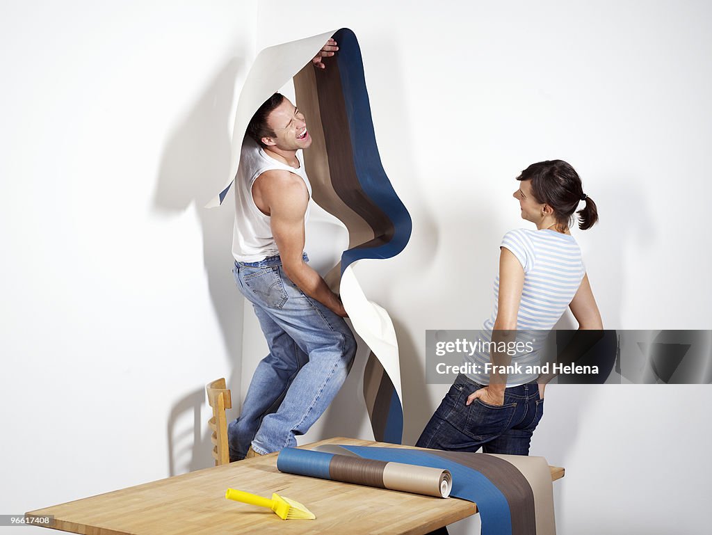 Smiling man struggling with wallpaper
