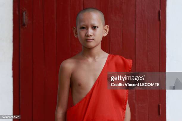 Vêtu de sa toge traditionnelle, un jeune apprenti pose devant la porte de son dortoir au temple bouddhiste de Vat Taohai à Luang Prabang, Laos, le 31...