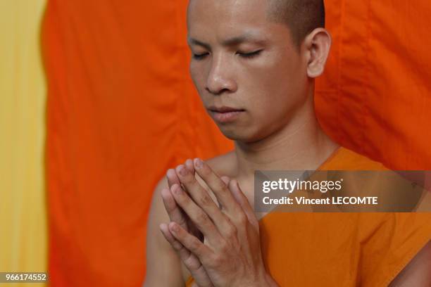 Vêtu de sa toge traditionnelle, mains jointes, un moine prie pendant la deuxième prière matinale au temple bouddhiste de Vat Taohai à Luang Prabang,...