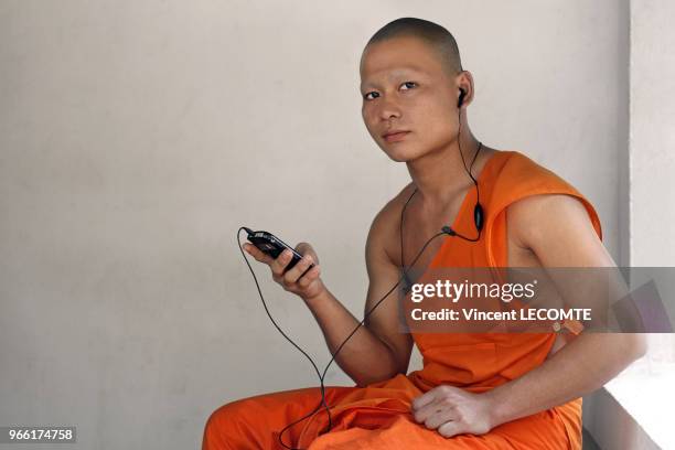 Un moine bouddhiste asiatique en tenue traditionnelle écoute de la musique avec son baladeur mp3 lors d?un moment de détente dans son sanctuaire...