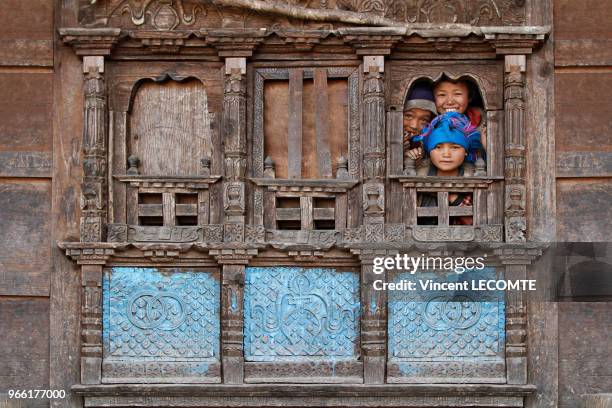 Trois enfants népalais regardant par la fenêtre de leur maison traditionnelle en bois dans le village de Chneding Ghyang, au Népal, le 19 avril 2012.