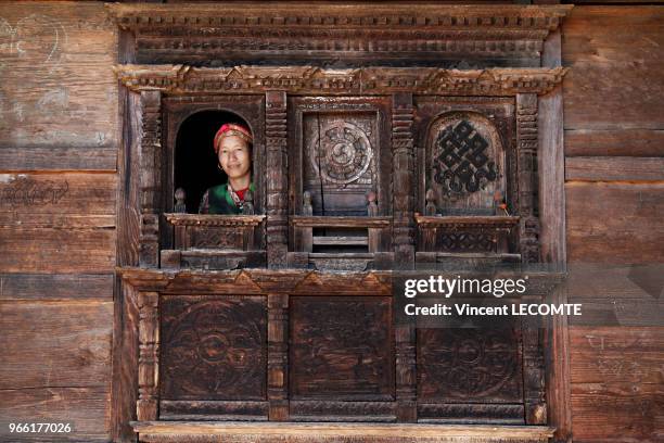 Villageoise népalaise regardant par la fenêtre de sa maison traditionnelle en bois dans le hameau de Brimdang, au Népal, le 22 avril 2012.