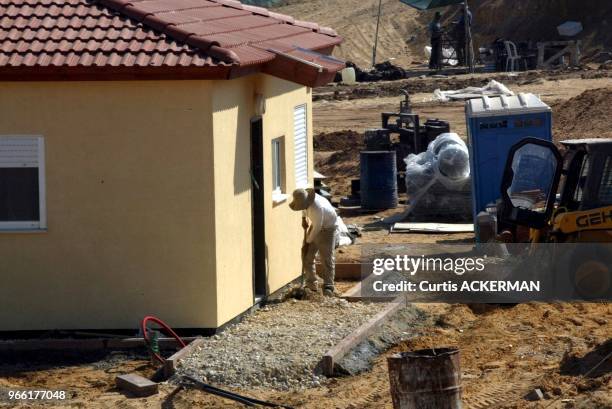 Worker spreads stone around the outside of a one of the finished pre-fabricated homes as part of a new shipment of 12 pre-fabricated homes, intended...