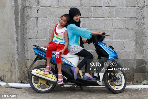 Adolescente indonésienne voilée et sa petite s?ur aux cheveux dénudés sur leur scooter à l'école de Basca à Painan, au sud de l?île de Sumatra, en...