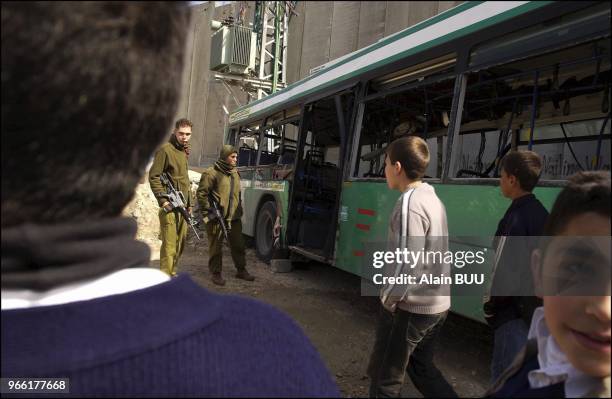 Palestinians children and Israeli soldiers near the remains of the bus targeted by a suicide bomb attack the day before was carried in front of the...