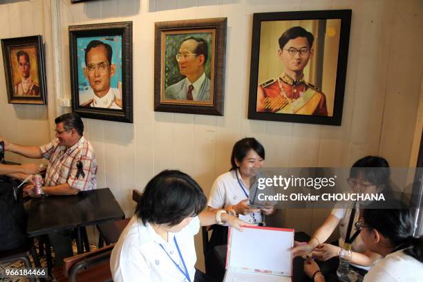 Jeunes thailandais et touristes prennant un verre dans un petit restaurant et café thailandais entièrement recouvert des portraits du roi de...