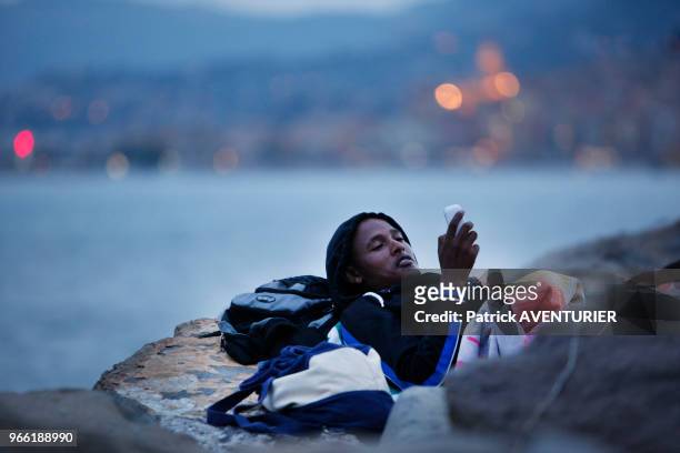 Migrant consultant un téléphone portable dans un camp de fortune sur des rochers à la frontière franco-italienne attendant de passer en territoire...