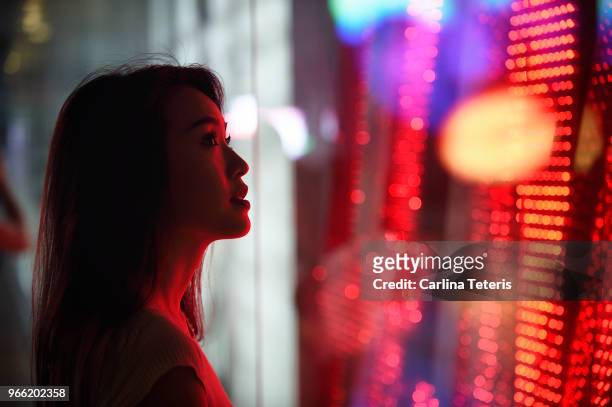 young woman standing next to a window with red light - verführung stock-fotos und bilder