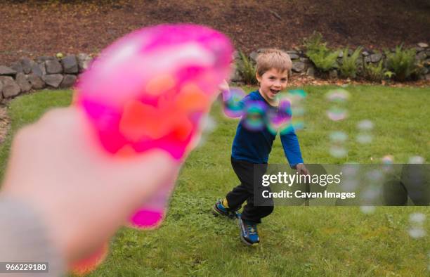 cropped image of hand holding bubble gun while playing with boy in yard - ungewöhnliche perspektive stock-fotos und bilder