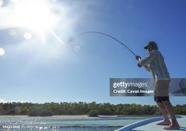 low angle view of man fishing while standing on boat deck against clear sky at caye caulker - the cayes stock pictures, royalty-free photos & images