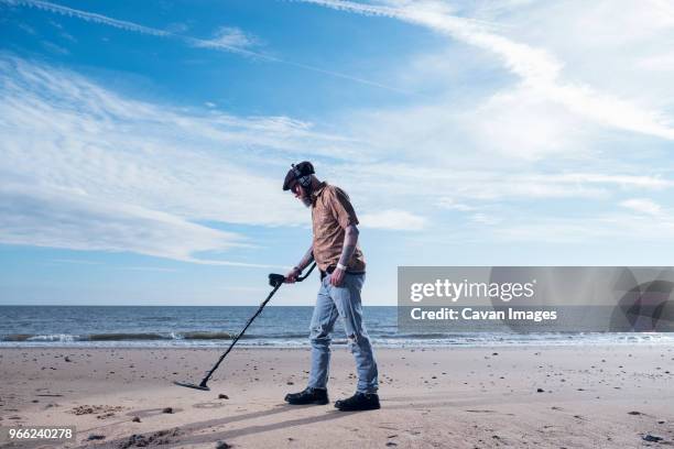 side view of man using recreational metal detector at horsey beach against sky - schatzoeken stockfoto's en -beelden