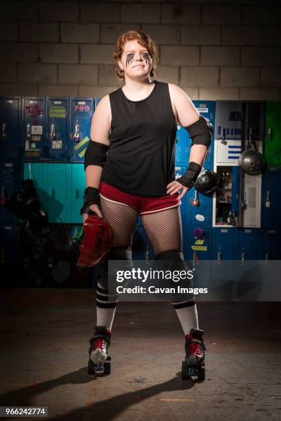 portrait of confident sportswoman with hand on hip wearing roller skates while standing against lockers - roller derby foto e immagini stock