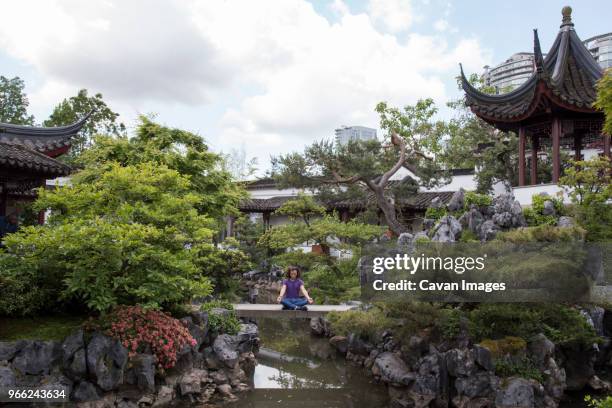 man meditating on footbridge over lake amidst chinese garden at sun yat-sen - chinesischer garten im klassischen stil stock-fotos und bilder