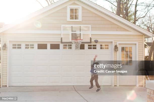 full length of boy playing basketball in drive way - garage driveway stock pictures, royalty-free photos & images