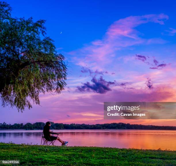 woman using mobile phone while relaxing at lakeshore against dramatic sky - lincoln nebraska foto e immagini stock