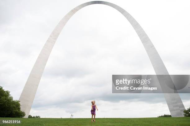 happy girl jumping on grassy field against gateway arch - gateway arch st louis stock pictures, royalty-free photos & images