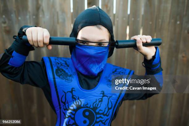 portrait of boy in ninja costume standing against wooden fence - ninja kid stock pictures, royalty-free photos & images