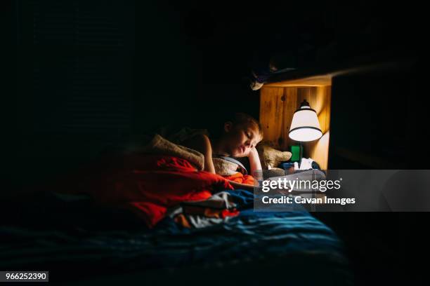 boy reading book in darkroom under electric lamp at home - dark room stock-fotos und bilder