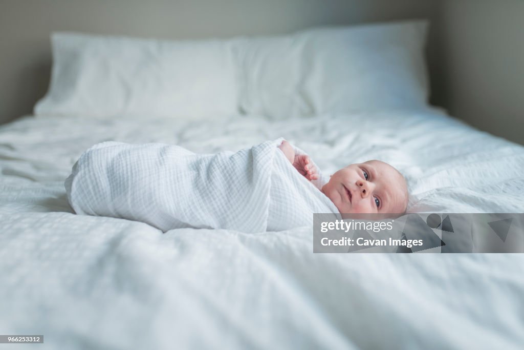 Side view of newborn baby boy looking away while lying in bed at home