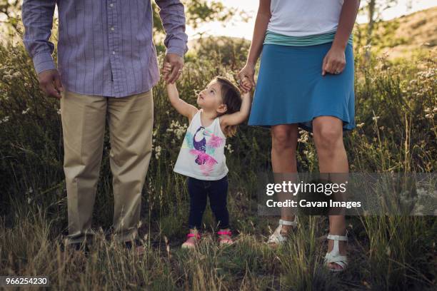 low section of parents holding hands of daughter while standing on grassy field - entre deux photos et images de collection